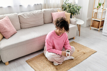 A young woman smiles while sipping a warm drink in her home.