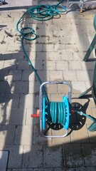 A hose rolled onto a reel for watering lawns stands on the ground in the garden.