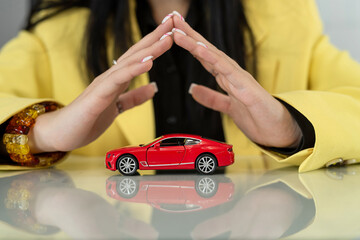 close up of businesswoman hand abobe red toy car. Protection of car or insurance