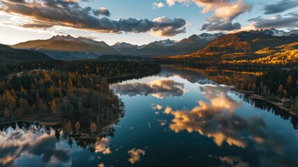 Fototapeta premium Panoramic aerial landscape on sunset over majestic lake in mountains with autumn colored forest around. Clouds in sky and trees reflect in water in lake