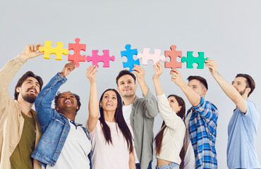 Happy smiling group of business people in casual clothes assembling wooden puzzle indoors. Company...