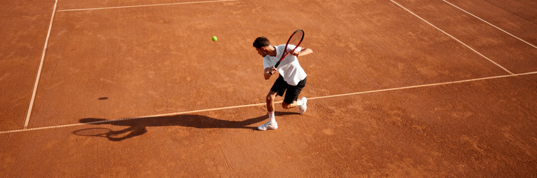 Tennis player, active man in sportwear in motion, training on clay court, displaying determination and strength. Concept of sport, competition, active and healthy lifestyle. Banner. Copy space for ad