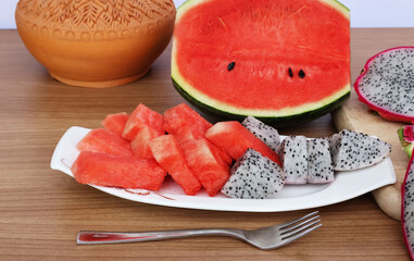 Watermelon and dragon fruit cut in a white porcelain plate and cut in half placed on the back on a wooden table with a white background.


