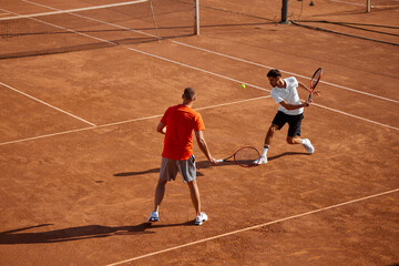Two men, tennis players in motion on outdoor clay court, showing game skills and teamwork cooperation, playing with focus. Concept of sport, competition, active and healthy lifestyle