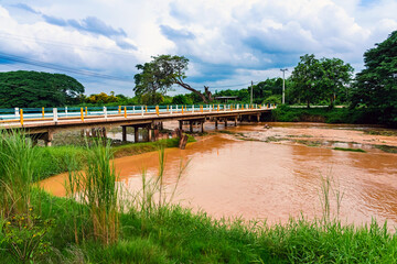 Fototapeta premium View of irrigation canal with weeds and debris flowing together with strong flowing dirty brown water due to soil and mud from forest after heavy rains and floods. La Nina crisis, Water pollution.
