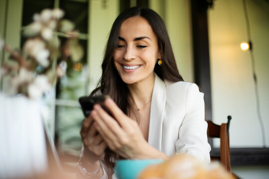 Modern successful independent confident beautiful business woman in a smart business suit using her phone sitting at a table in a summer city cafe in a good mood