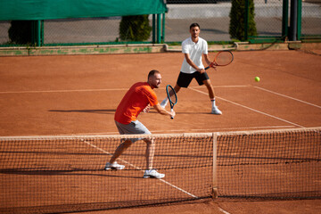 Dynamic image of two men, professional tennis players in motion on clay court, training before important game. Team mates. Concept of sport, competition, active and healthy lifestyle