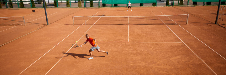 Dynamic scene of two competitive men, professional tennis players engaged in intense game on outdoor clay court. Concept of sport, competition, active and healthy lifestyle. Banner