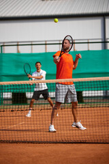 Obraz premium Team of court. Two focused men, tennis players playing with concentration on clay court, showing dynamic skills and good coordination. Concept of sport, competition, active and healthy lifestyle