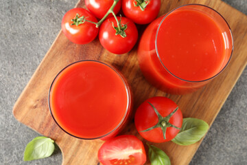 Tasty tomato juice in glasses, basil and fresh vegetables on grey table, top view