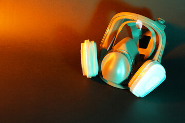 One respirator mask on dark background in orange light, top view and space for text. Safety...