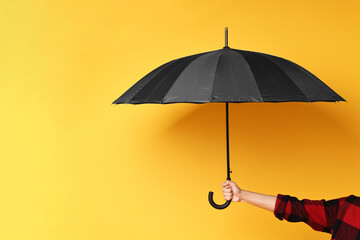 Man holding black umbrella on yellow background, closeup