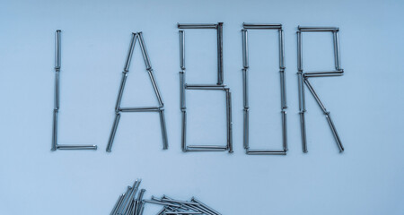 The word labor is laid out from nails of different sizes on a gray background.