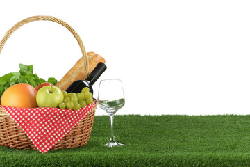Picnic wicker basket with food, bottle of wine and glass on grass against white background. Space for text