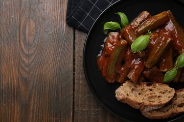 Tasty stew with okra, tomato sauce, bread and basil on wooden table, top view. Space for text