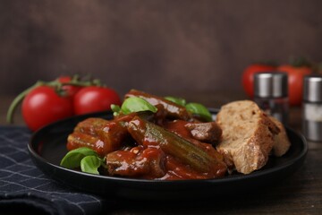 Tasty stew with okra, tomato sauce, bread and basil on wooden table, closeup