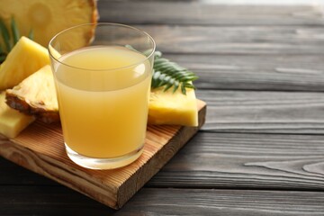 Tasty pineapple juice in glass and slices of fresh fruit on wooden table, closeup. Space for text
