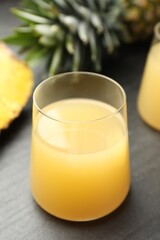 Tasty pineapple juice in glass and fruit on grey textured table, closeup