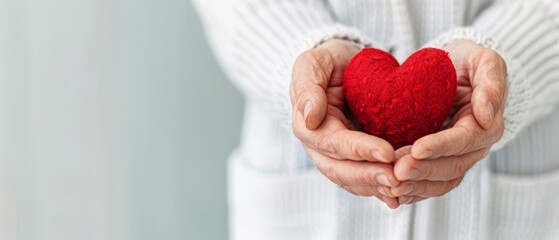 A person closely holds a red heart in their palms, wearing a white sweater