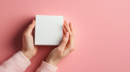 Obraz premium Female hands holding a white blank box on a pastel pink background.