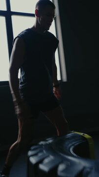 Man focusing on lifting a heavy tire in a dimly lit gym, showcasing strength, focus, and determination in this intense workout session. Perfect for fitness and bodybuilding themes. Vertical