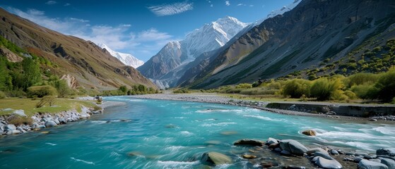 Obraz premium A river runs through a verdant valley, surrounded by snow-capped mountains and trees