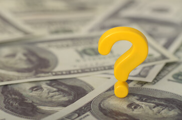 The image depicts a yellow question mark resting on a bed of 100-dollar bills, symbolizing...