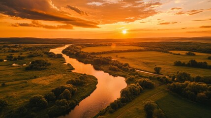 An aerial view of a river snaking through a lush green valley, bathed in the warm glow of a setting sun, with a dramatic, fiery orange sky.