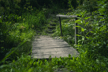 Wooden, old bridge over a narrow river in the village. Thick grass