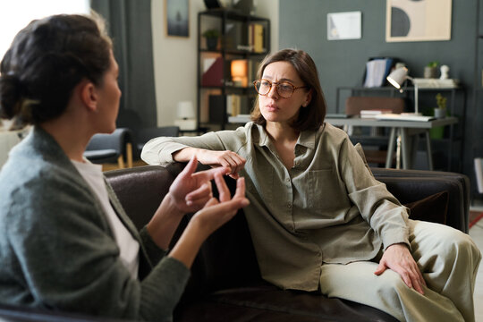 Two women are intently discussing mental health in a counseling session Both are seated on a comfortable couch in a cozy, well-decorated room surrounded by books and personal items