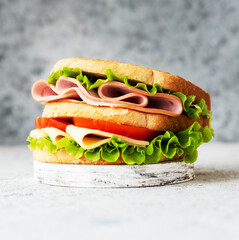 Tower sandwich of white bread, cheese, ham and lettuce with tomato, close-up. Light background.