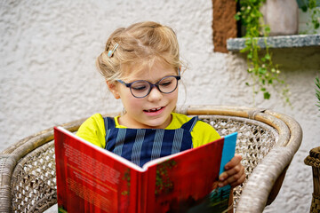 Little girl with eyeglasses reading book. Happy interested child learning.