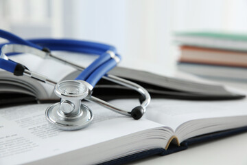 One medical stethoscope and books on white table, closeup