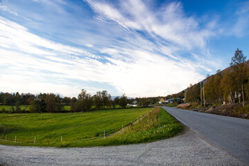 TROMSO, NORWAY - SEPTEMBER 17, 2014: Scenic countryside in Tromsø, Norway, during a beautiful sunny day. Asphalt road along green fields and trees on the side of the road.