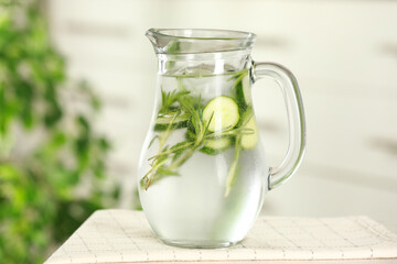 Refreshing cucumber water with rosemary in jug on white table, closeup