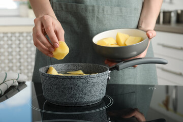 Woman putting potato into saucepan on stove, closeup