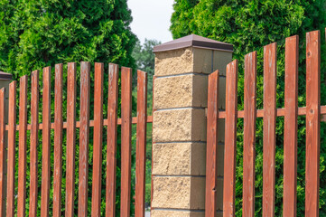 Fence with wooden panels and brick wall on yard grounds. Brown straight picket fence and light...