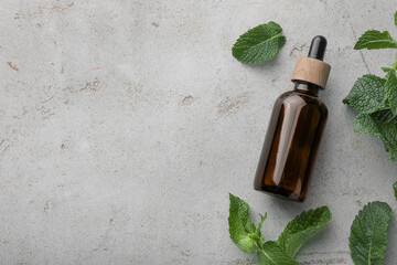 Bottle of essential oil and mint on light textured table, flat lay. Space for text