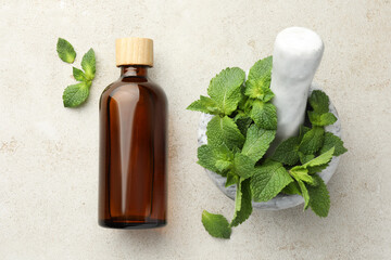 Bottle of essential oil, mint, mortar and pestle on light textured table, top view