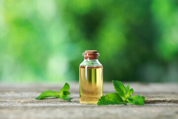 Bottle of mint essential oil and fresh leaves on wooden table
