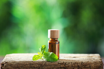 Bottle of mint essential oil and fresh leaves on wooden table