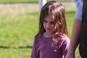 A little cute red-haired girl holds her mother's hand while standing against a background of green grass. 