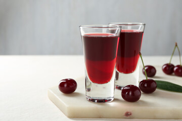 Delicious cherry liqueur in shot glasses and berries on white table, closeup. Space for text