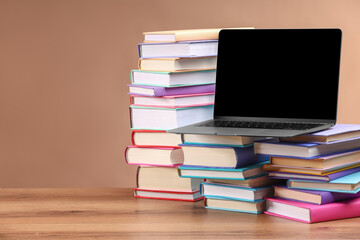 Stacks of colorful books and laptop on wooden table against light brown background, space for text