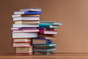 Stacks of colorful books on wooden table against light brown background, space for text