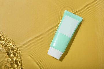 Tube with cream in water on yellow background, top view. Cosmetic product