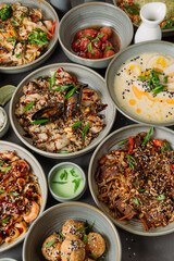 Variety of asian food dishes with seafood, noodles, meat and sesame seeds being served on gray table