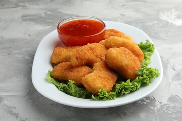 Tasty chicken nuggets with chili sauce and lettuce on grey textured table