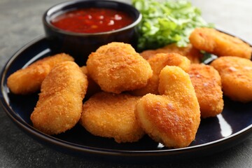 Tasty chicken nuggets with chili sauce on grey table, closeup