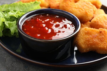 Chili sauce with tasty chicken nuggets on grey table, closeup